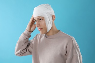 Photo of Man with head wrapped in medical bandage on light blue background