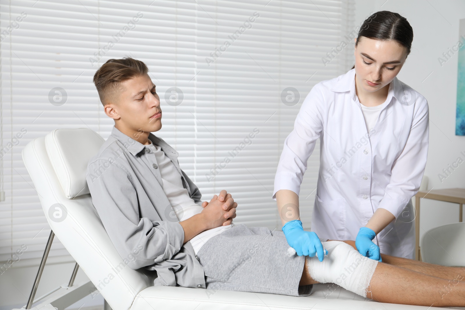 Photo of Doctor applying bandage onto patient's knee in clinic