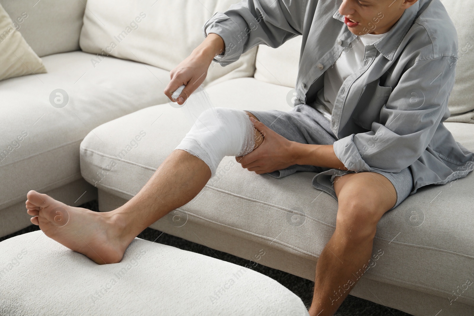 Photo of Man wrapping knee in medical bandage on sofa at home, closeup