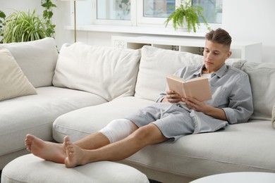 Photo of Man with medical bandage on his knee reading at home