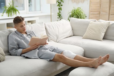 Photo of Man with medical bandage on his knee reading at home