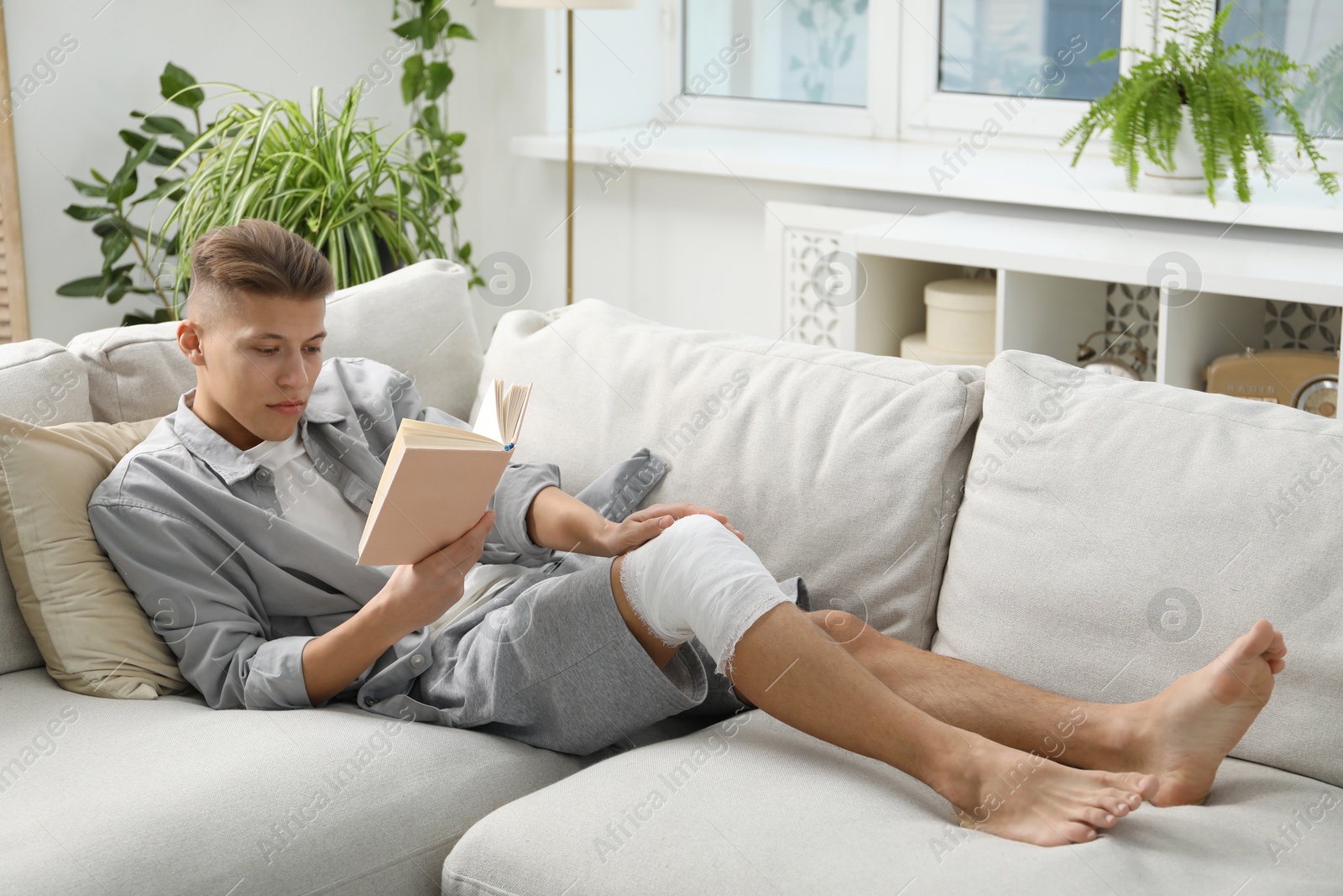 Photo of Man with medical bandage on his knee reading at home