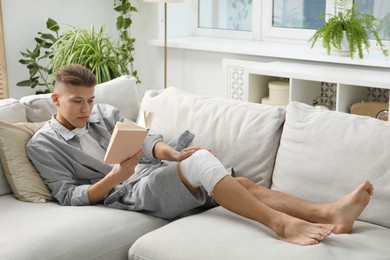 Photo of Man with medical bandage on his knee reading at home