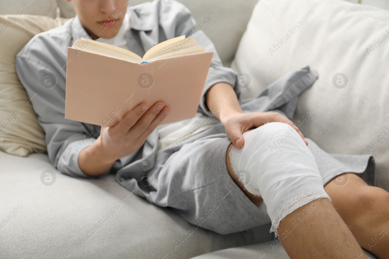 Photo of Man with medical bandage on his knee reading at home, closeup