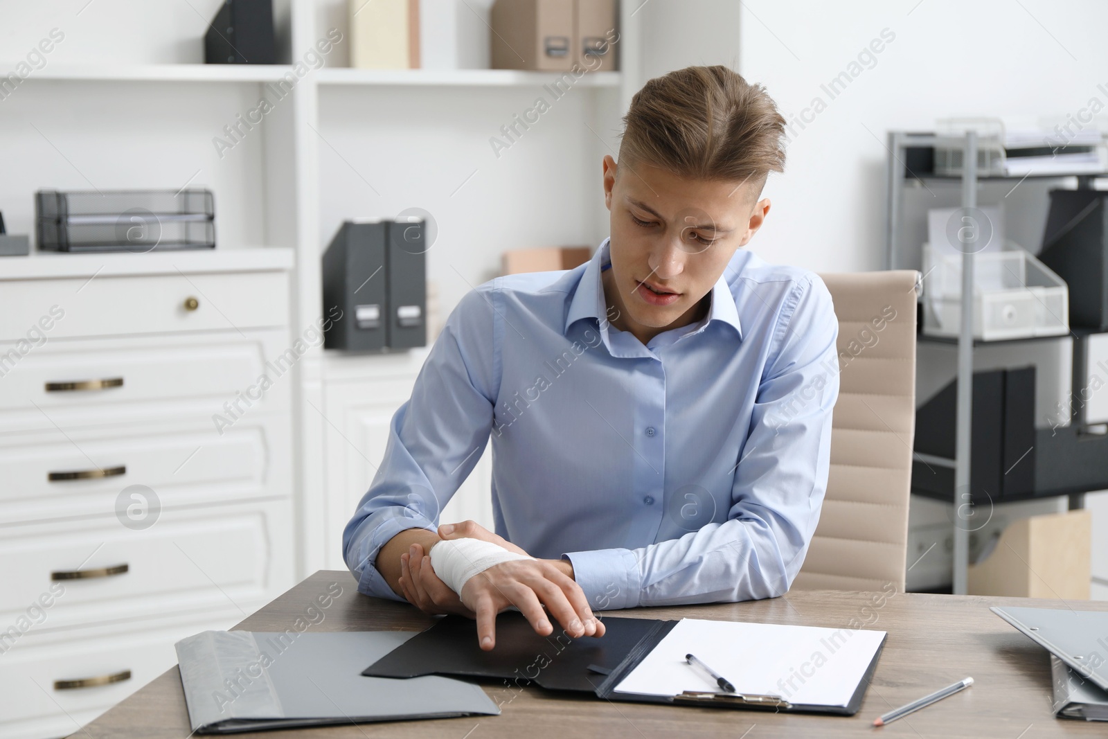 Photo of Man with medical bandage on his wrist at wooden table indoors