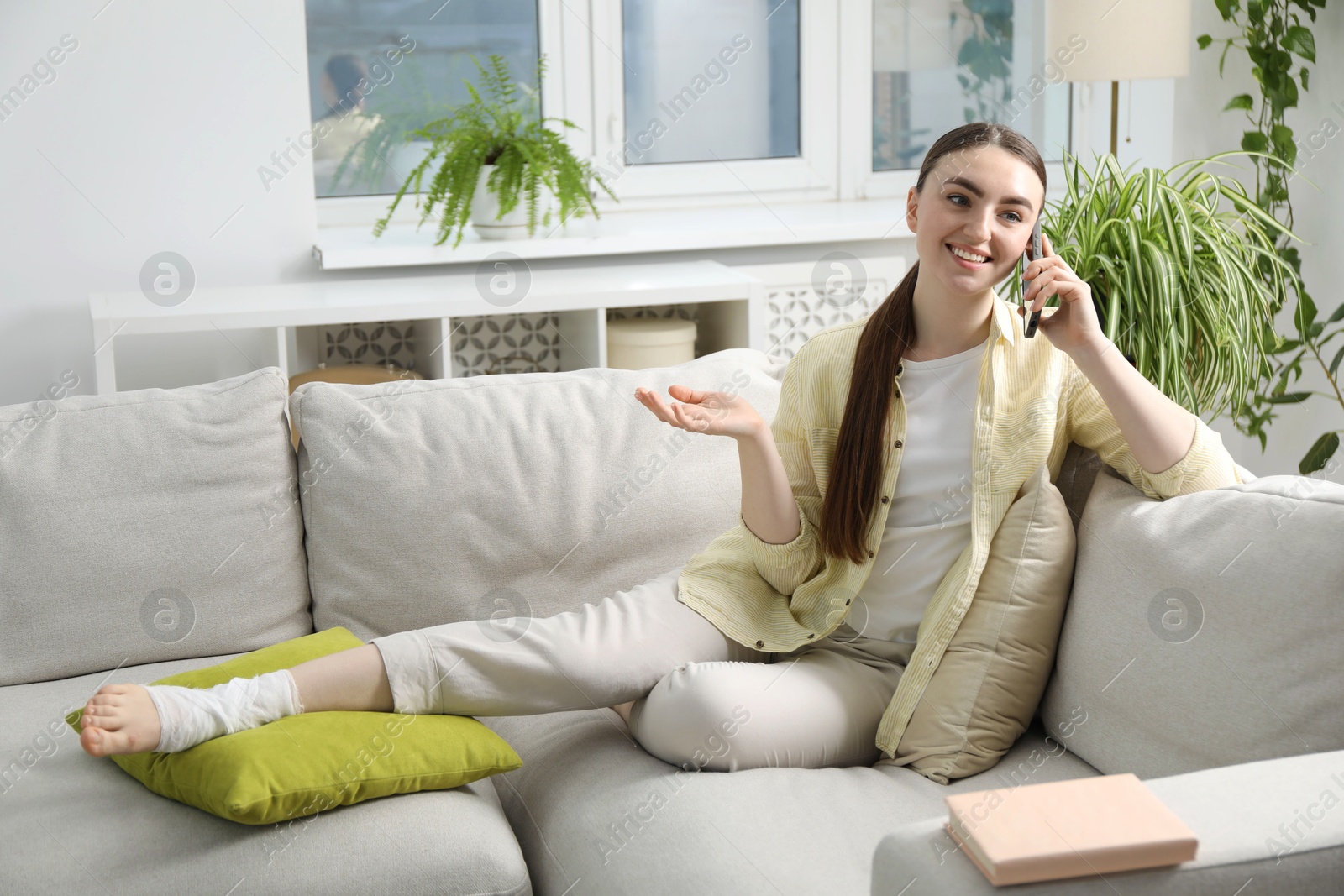 Photo of Woman with foot wrapped in medical bandage talking on smartphone at home