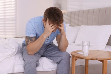 Unhappy young man suffering from hangover on bed at home