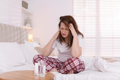 Unhappy woman suffering from hangover on bed at home