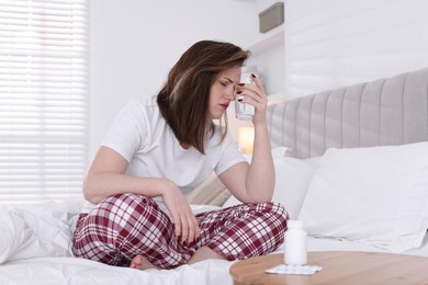 Photo of Unhappy woman with glass of water suffering from hangover on bed at home