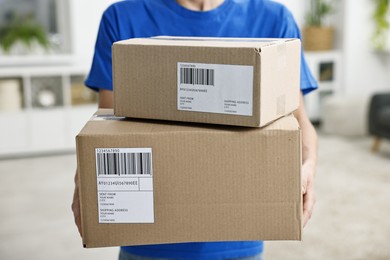 Photo of Man holding parcels with shipping labels indoors, closeup