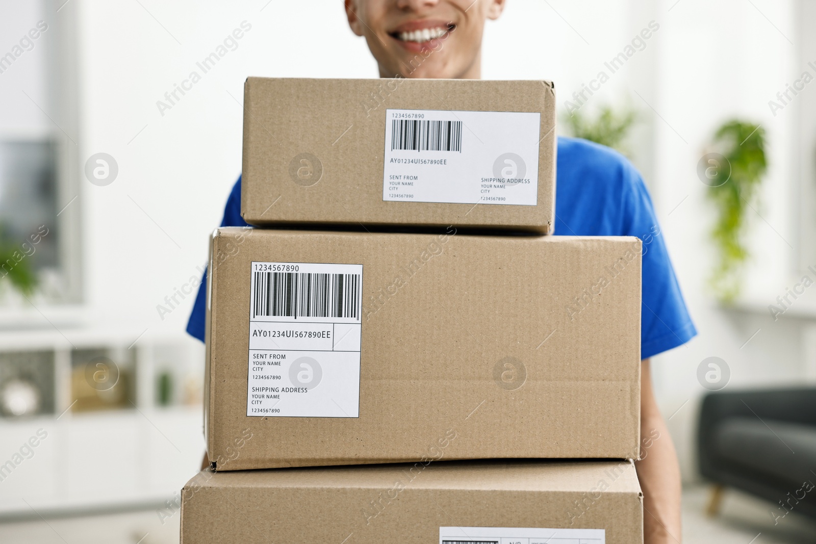 Photo of Man holding parcels with shipping labels indoors, closeup