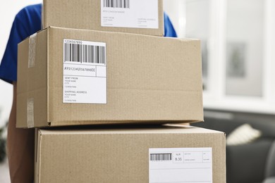 Photo of Man holding parcels with shipping labels indoors, closeup