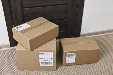 Photo of Cardboard parcel boxes with shipping labels near door indoors