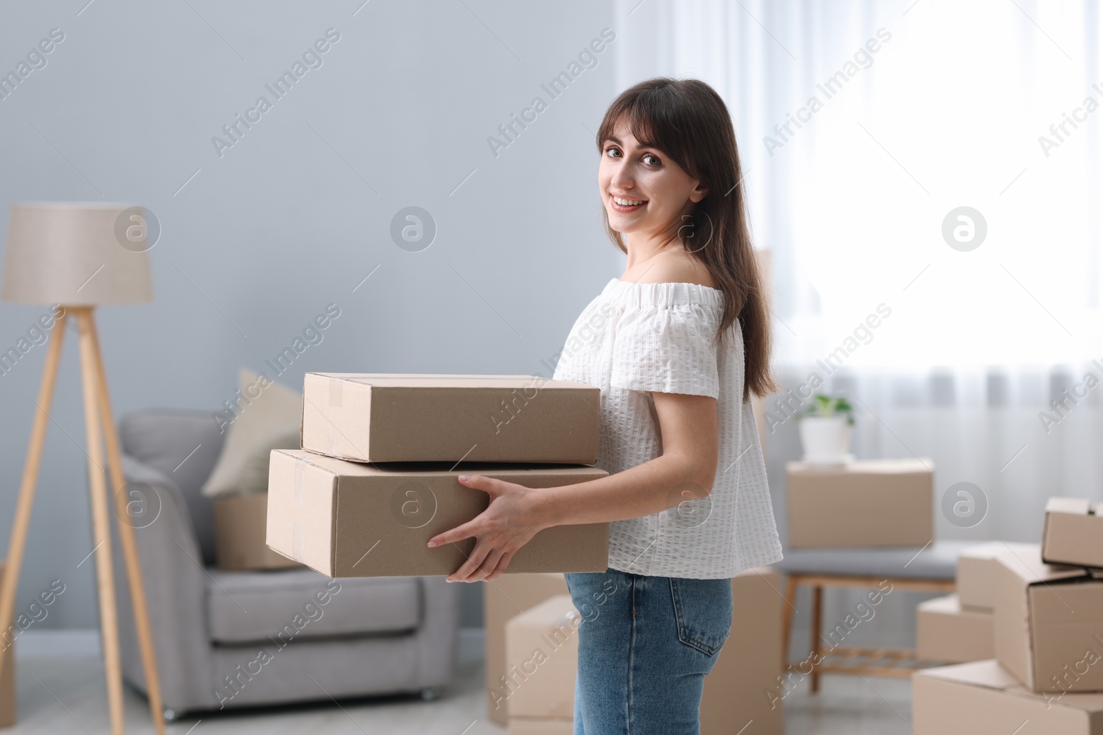 Photo of Moving day. Happy woman with cardboard boxes in her new home