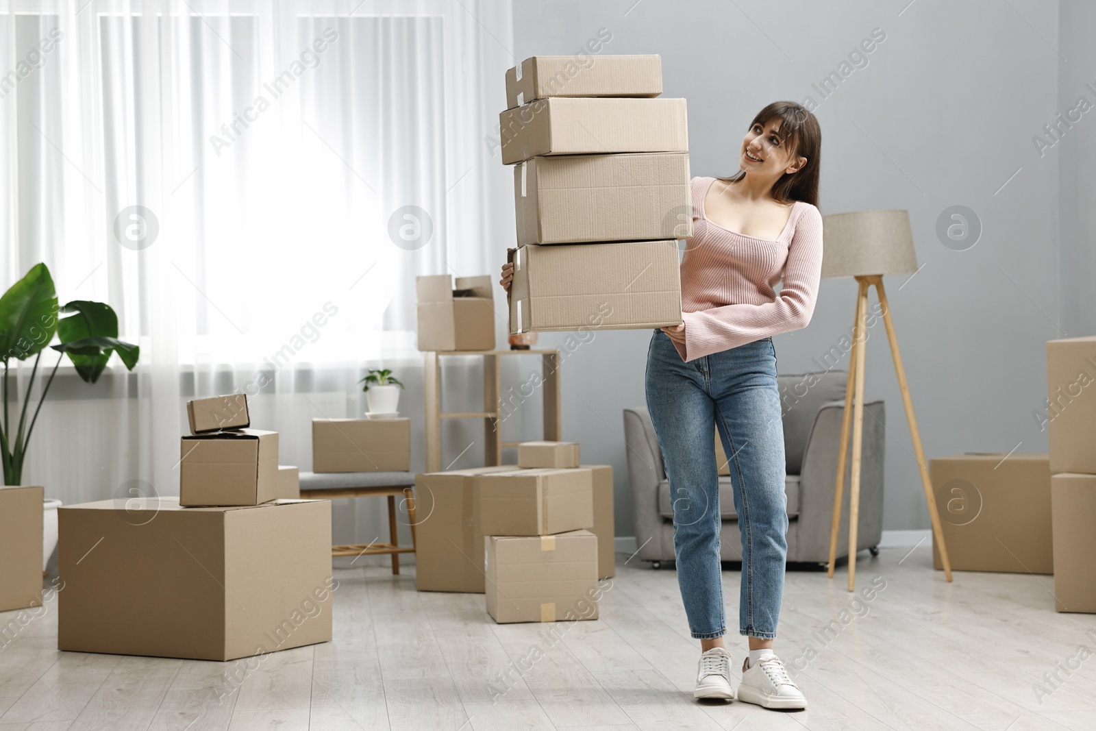 Photo of Moving day. Happy woman with cardboard boxes in her new home