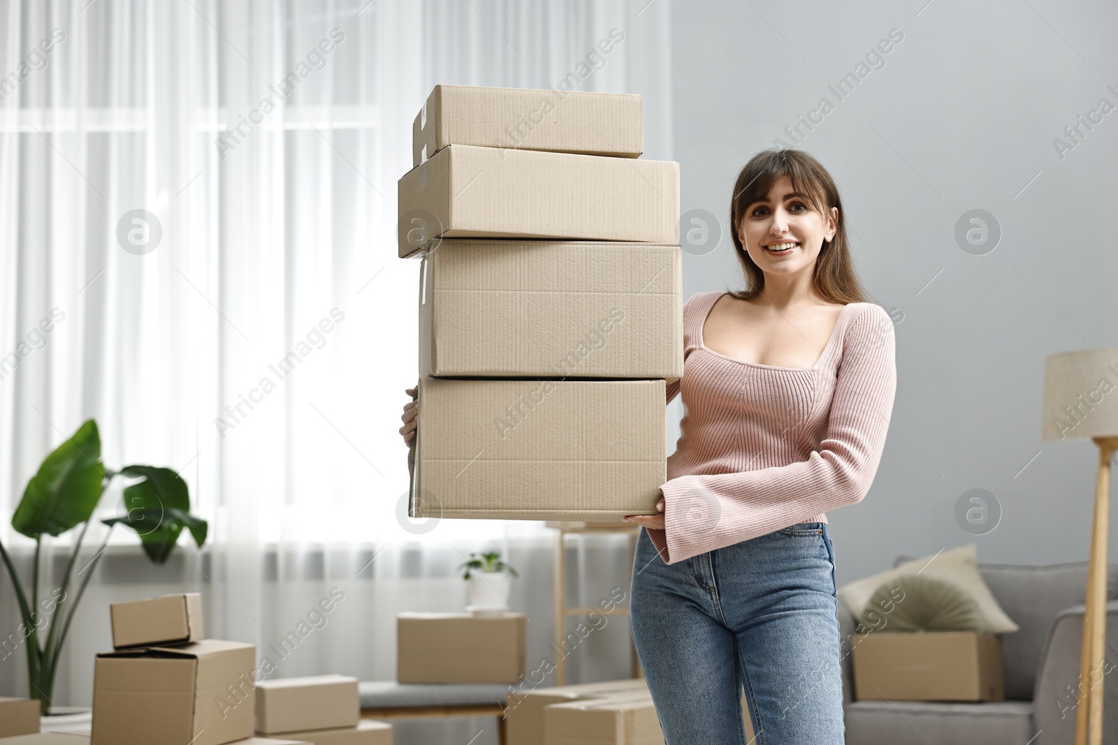 Photo of Moving day. Happy woman with cardboard boxes in her new home