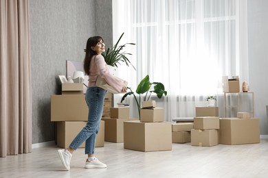 Photo of Moving day. Happy woman with cardboard box and houseplant in her new home