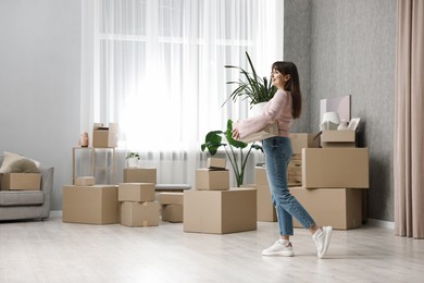 Moving day. Happy woman with cardboard box and houseplant in her new home