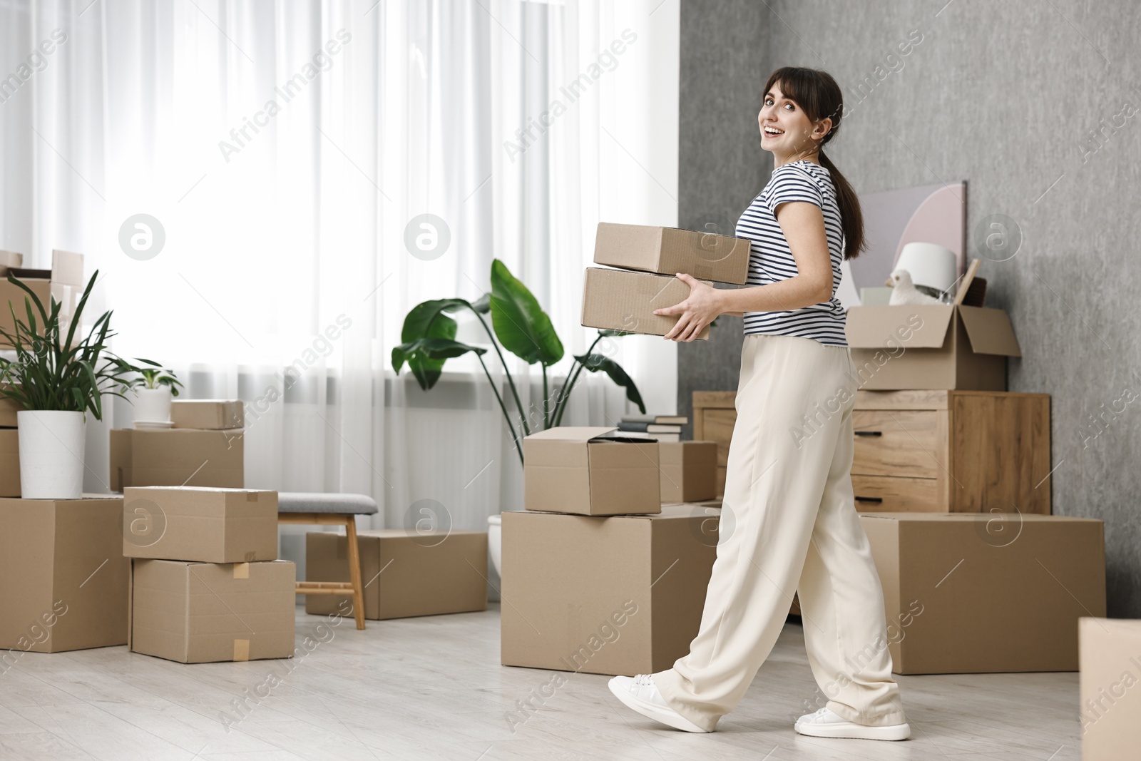 Photo of Moving day. Happy woman with cardboard boxes in her new home