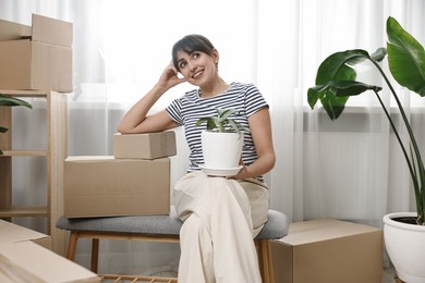 Moving day. Happy woman with houseplant and cardboard boxes in her new home