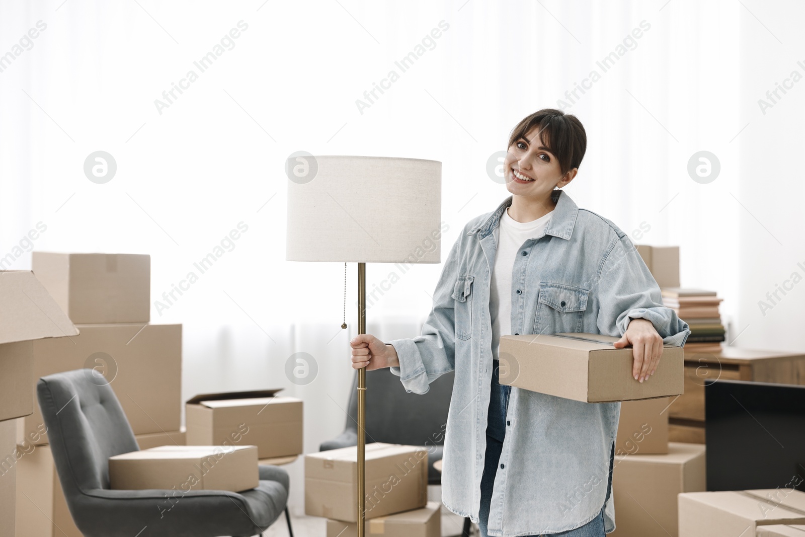 Photo of Moving day. Happy woman with lamp and cardboard box in her new home