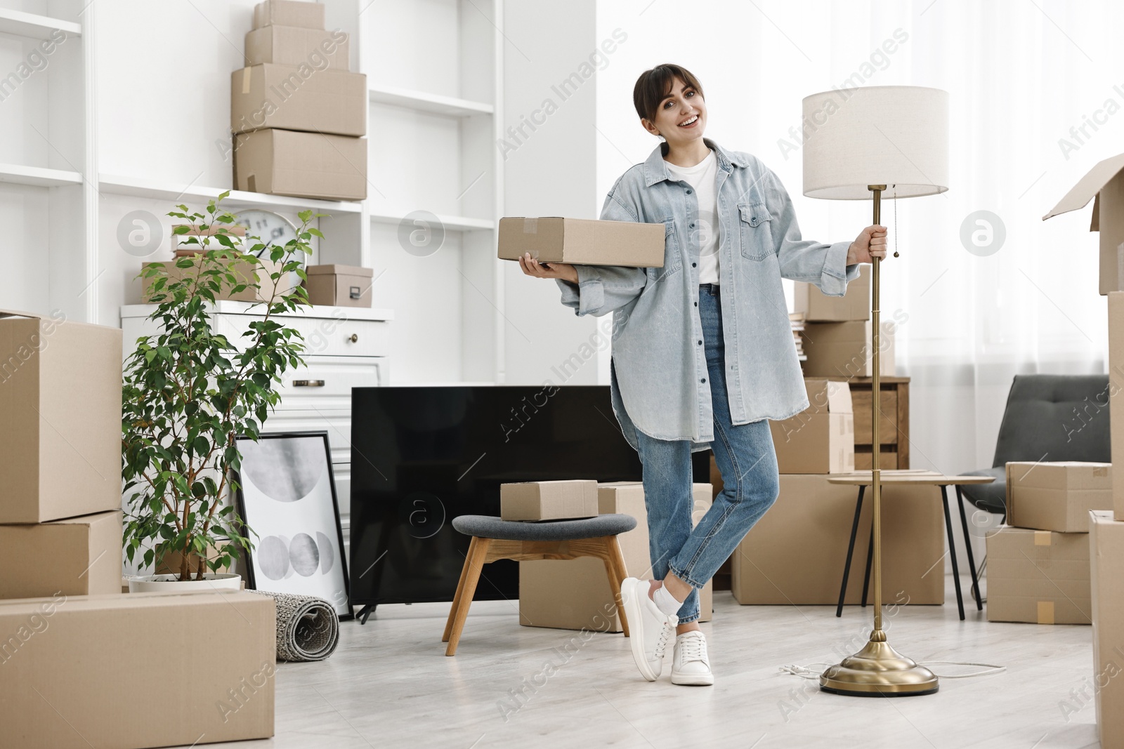 Photo of Moving day. Happy woman with lamp and cardboard box in her new home