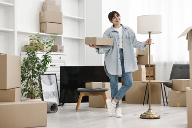 Moving day. Happy woman with lamp and cardboard box in her new home