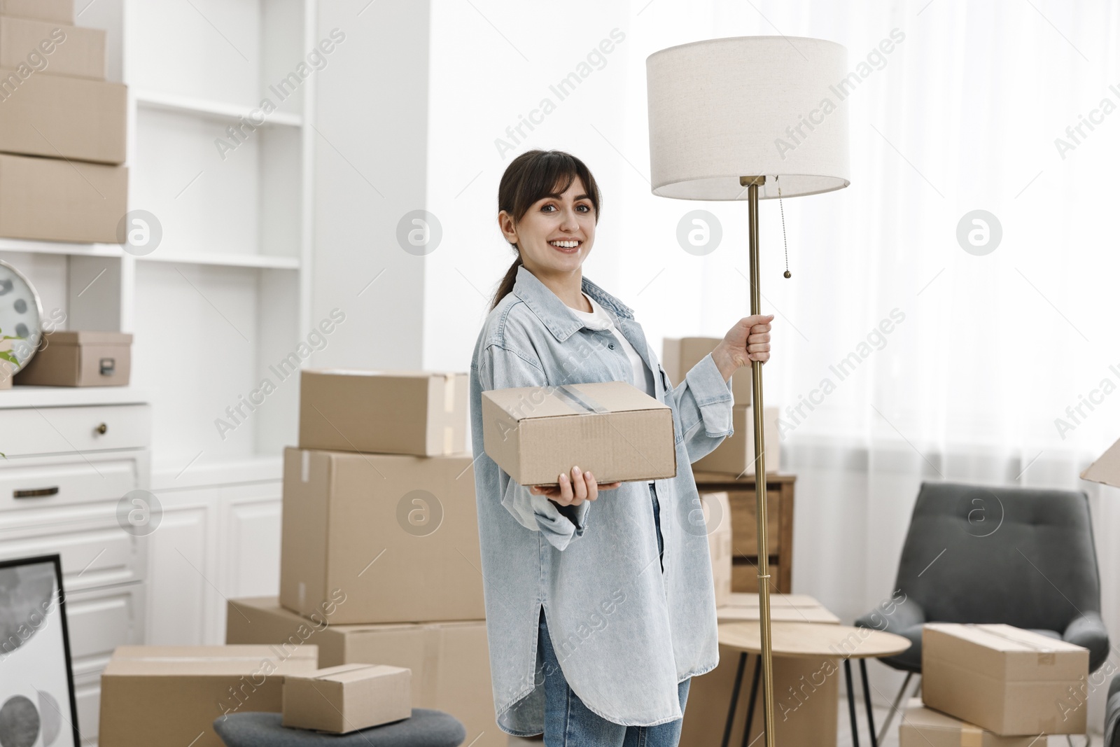 Photo of Moving day. Happy woman with lamp and cardboard box in her new home