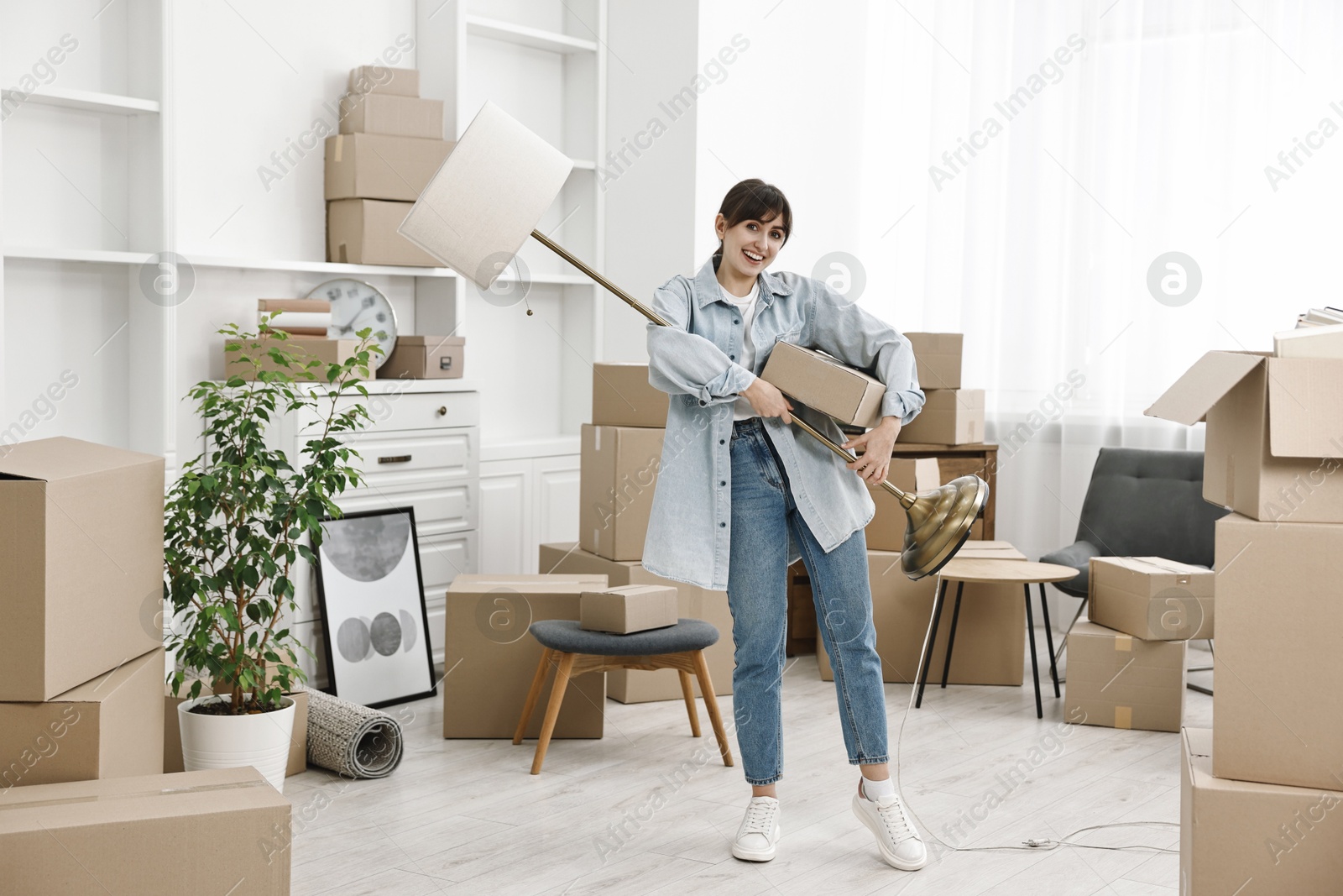 Photo of Moving day. Happy woman with lamp and cardboard box in her new home