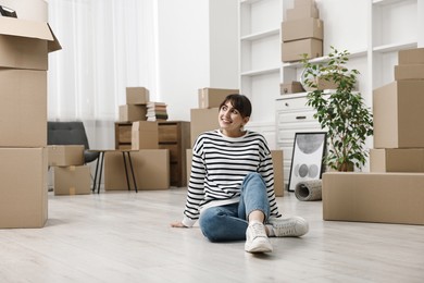 Photo of Moving day. Happy woman resting on floor and cardboard boxes in her new home