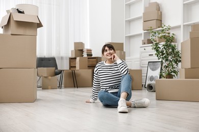 Photo of Moving day. Happy woman resting on floor and cardboard boxes in her new home