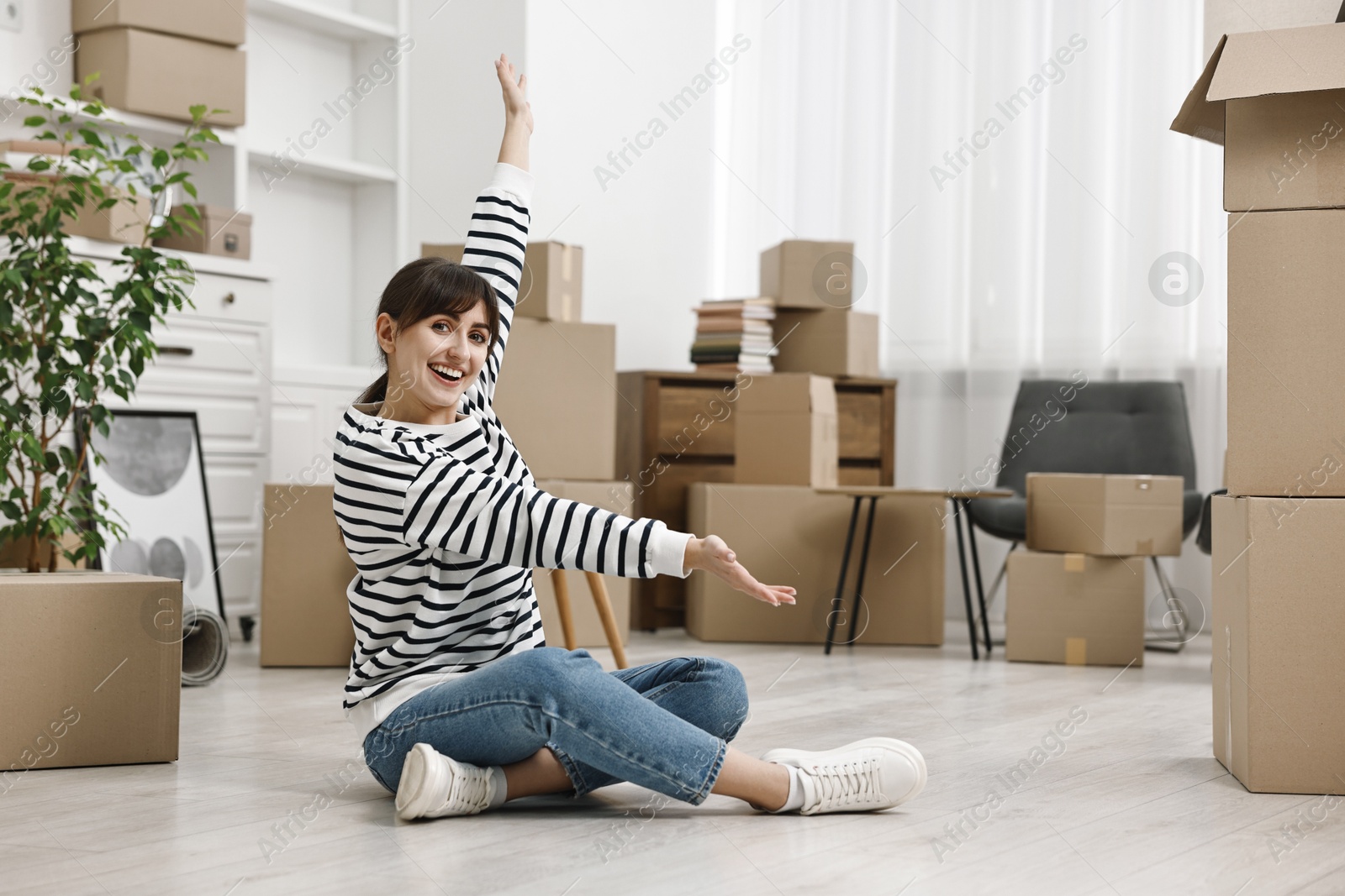 Photo of Moving day. Happy woman resting on floor and cardboard boxes in her new home