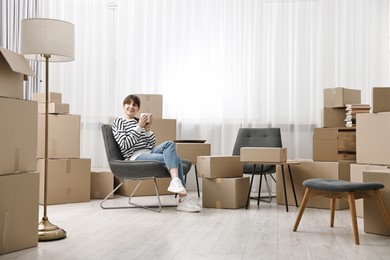 Moving day. Happy woman with cup of drink and cardboard boxes in new home