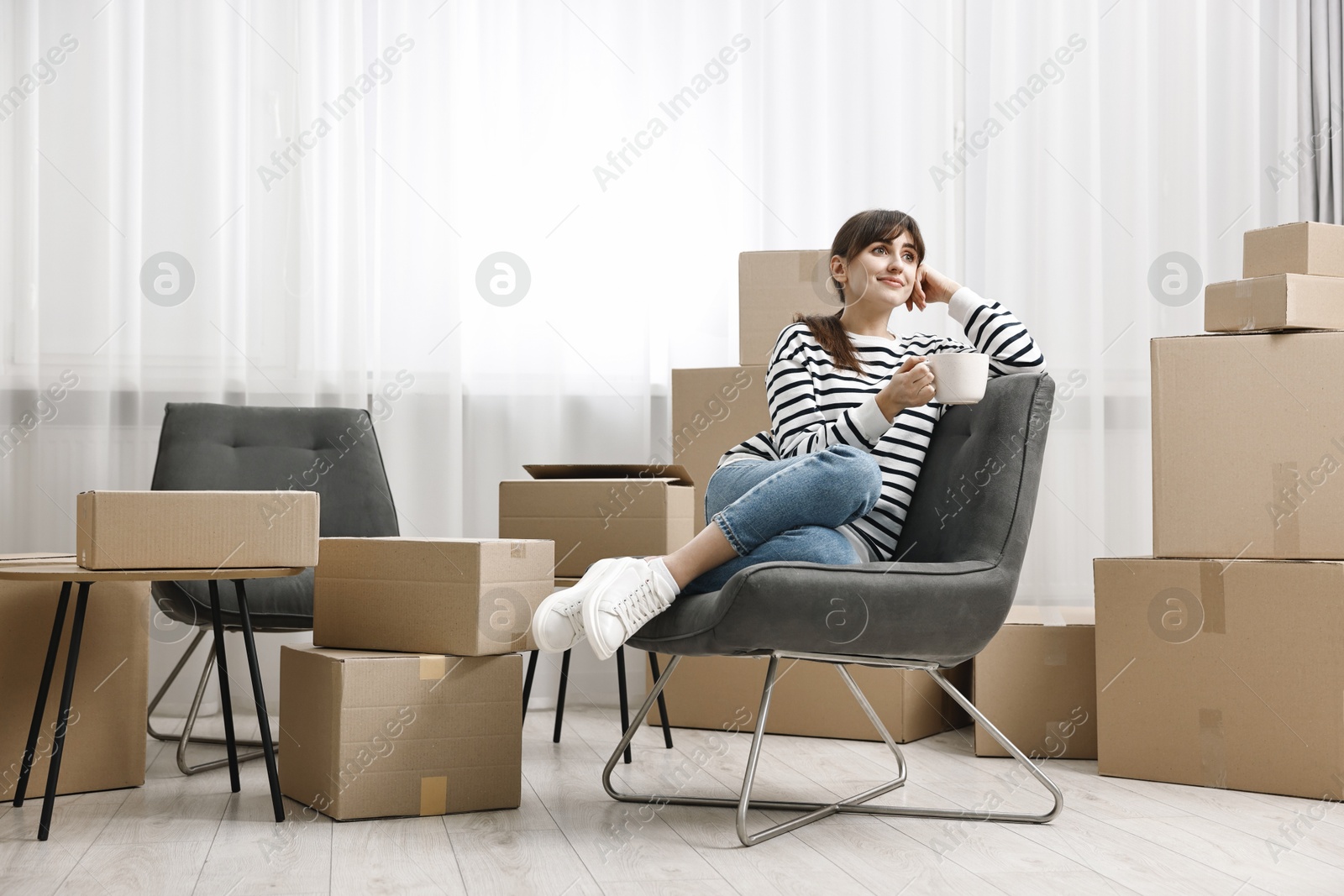 Photo of Moving day. Woman with cup of drink and cardboard boxes in new home