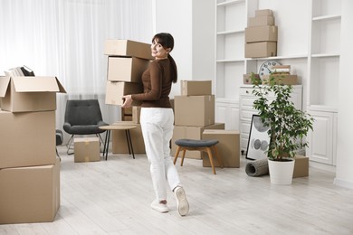 Photo of Moving day. Happy woman with cardboard boxes in her new home