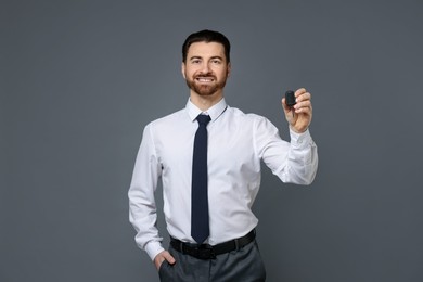 Cheerful salesman with car key on grey background