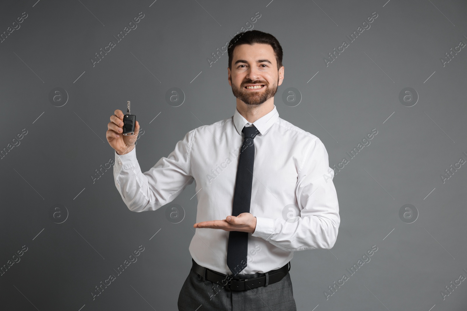 Photo of Cheerful salesman showing car key on grey background