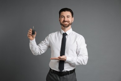 Photo of Cheerful salesman showing car key on grey background