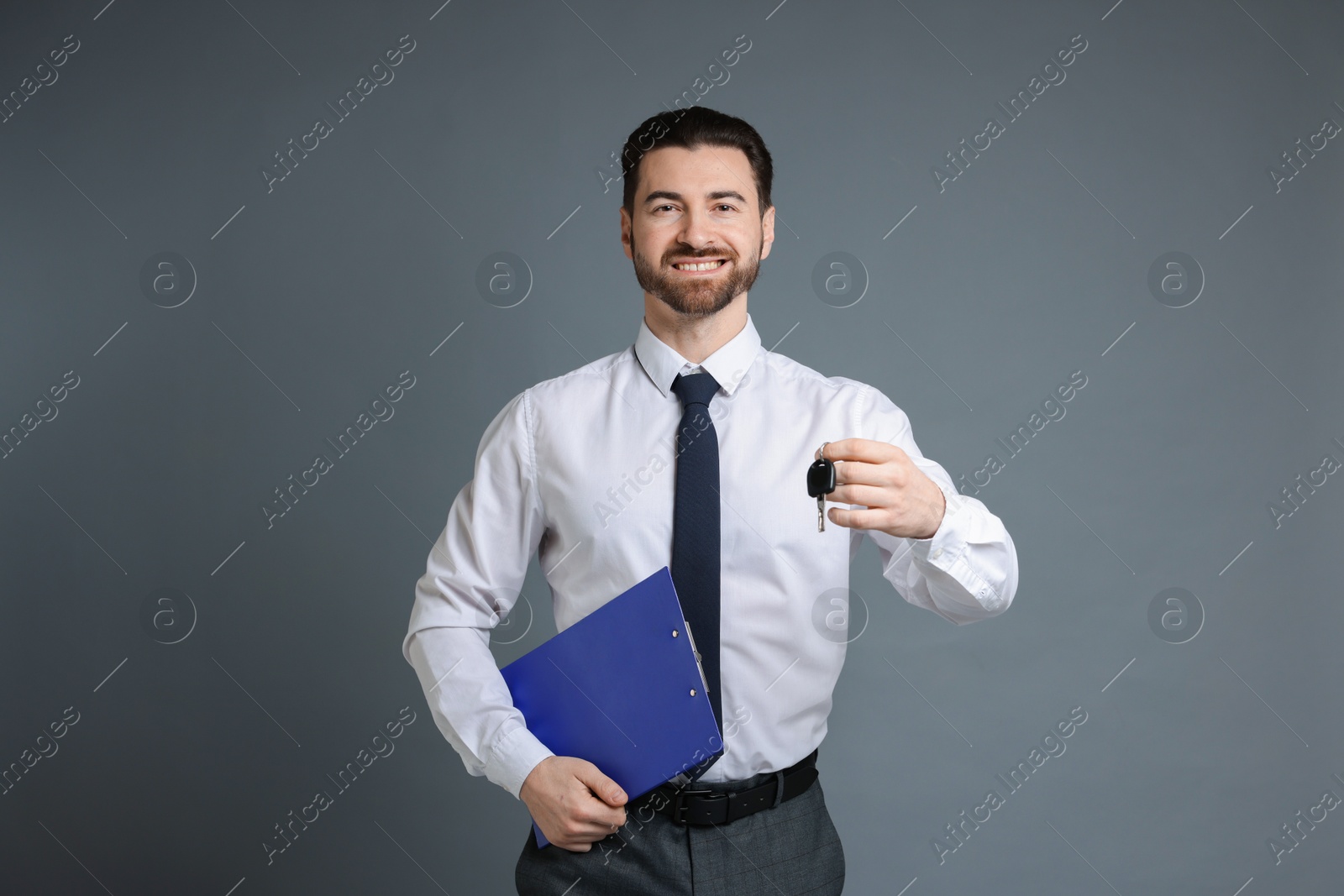 Photo of Cheerful salesman with car key and clipboard on grey background