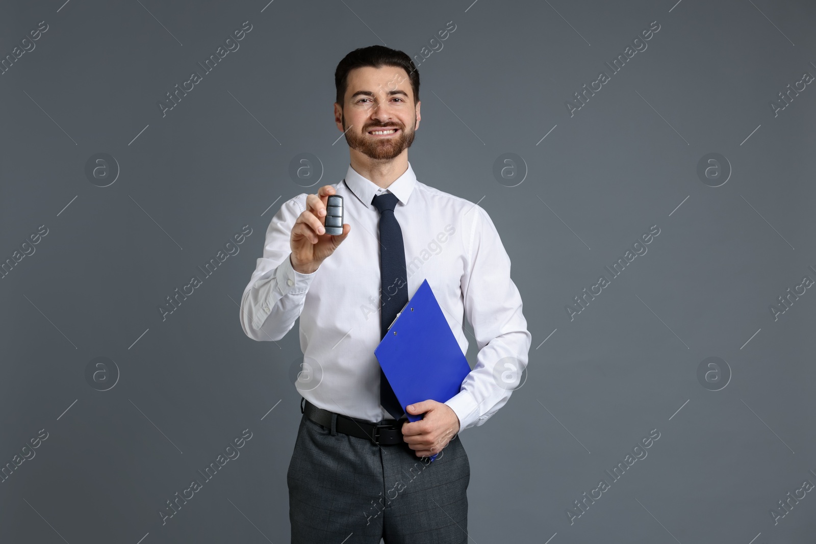 Photo of Cheerful salesman with car key and clipboard on grey background