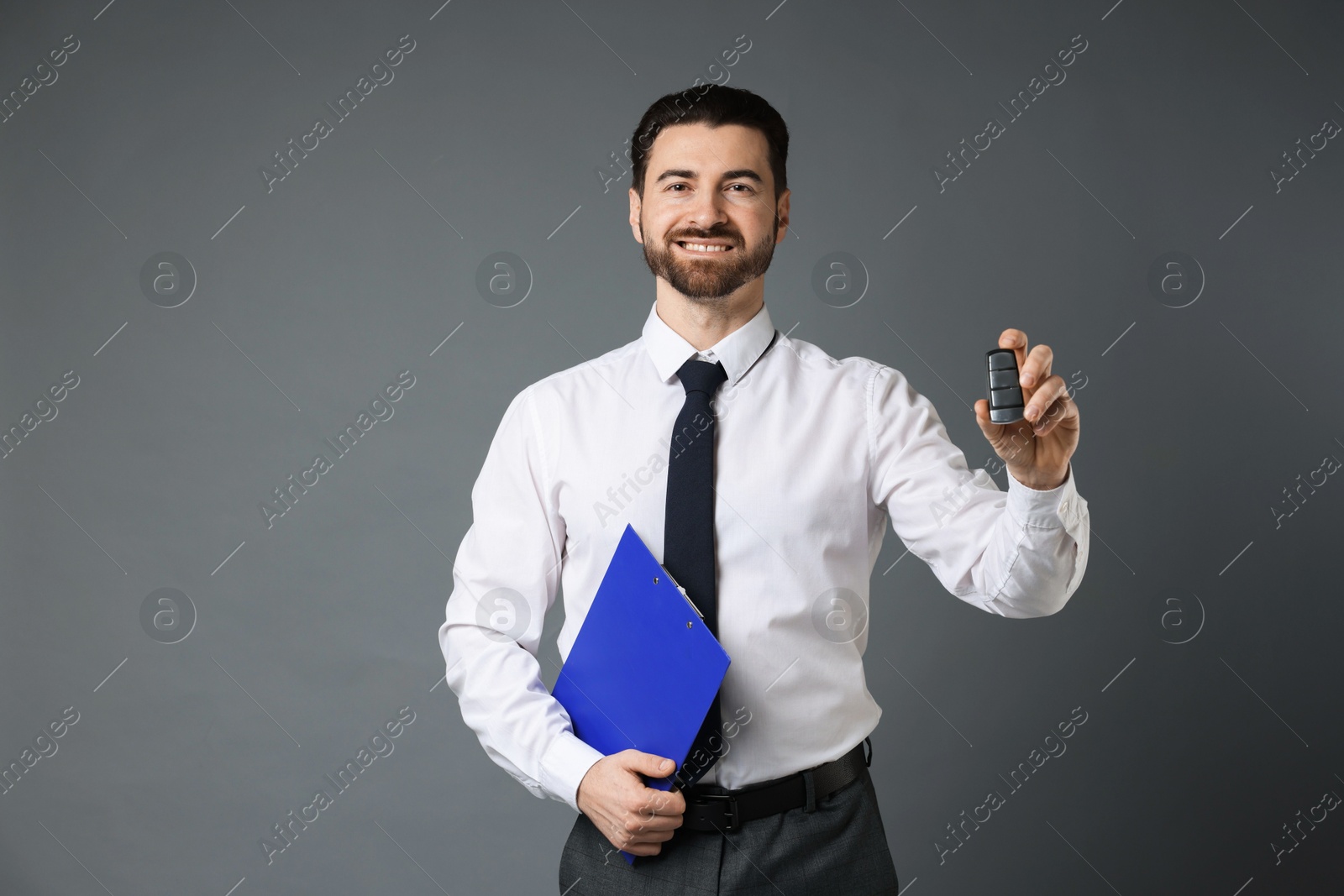 Photo of Cheerful salesman with car key and clipboard on grey background