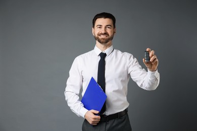 Photo of Cheerful salesman with car key and clipboard on grey background