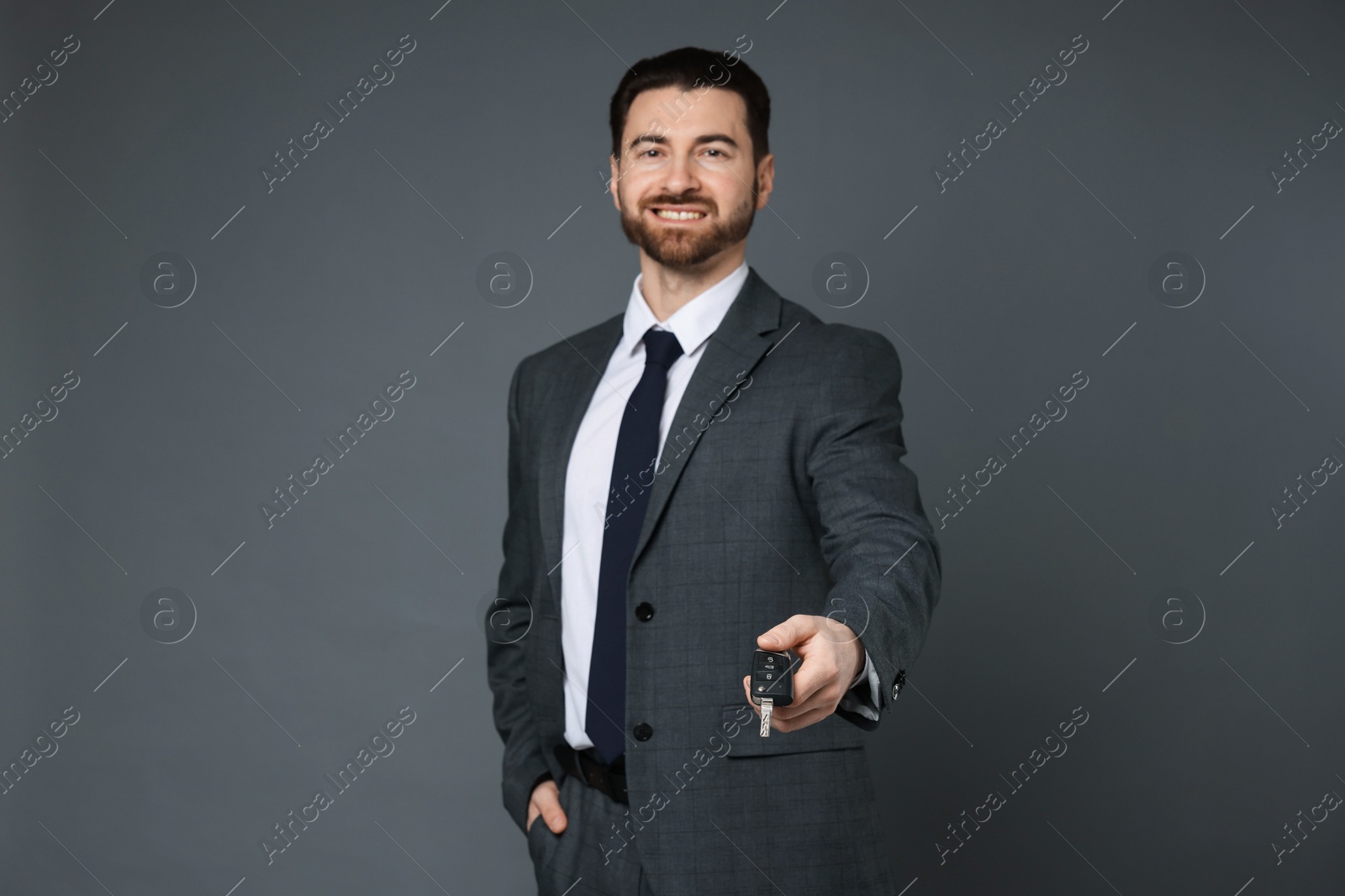 Photo of Cheerful salesman with car key on grey background