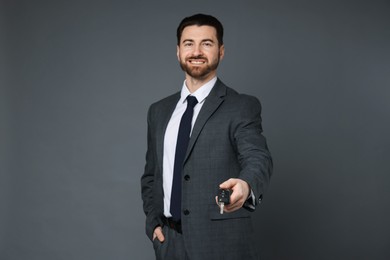 Cheerful salesman with car key on grey background