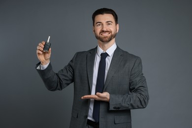 Photo of Cheerful salesman showing car key on grey background