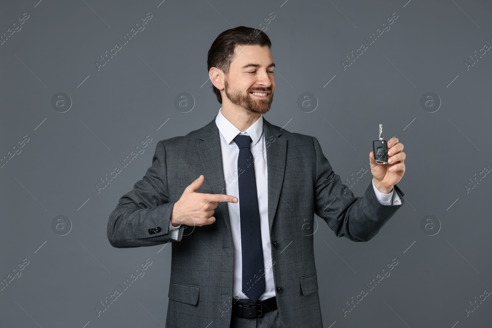 Photo of Cheerful salesman pointing at car key on grey background