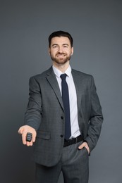 Cheerful salesman with car key on grey background