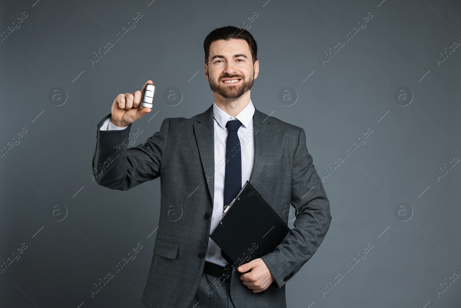 Photo of Cheerful salesman with car key and clipboard on grey background