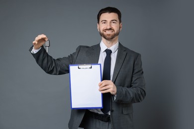 Photo of Cheerful salesman with car key and clipboard on grey background