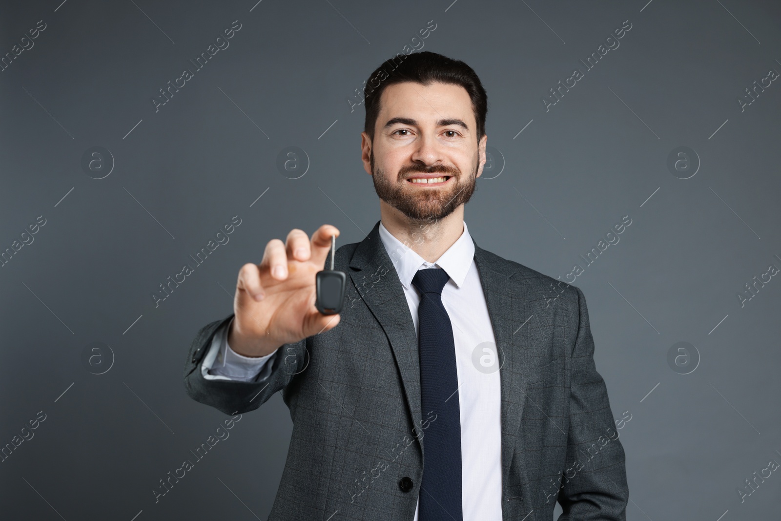 Photo of Cheerful salesman with car key on grey background